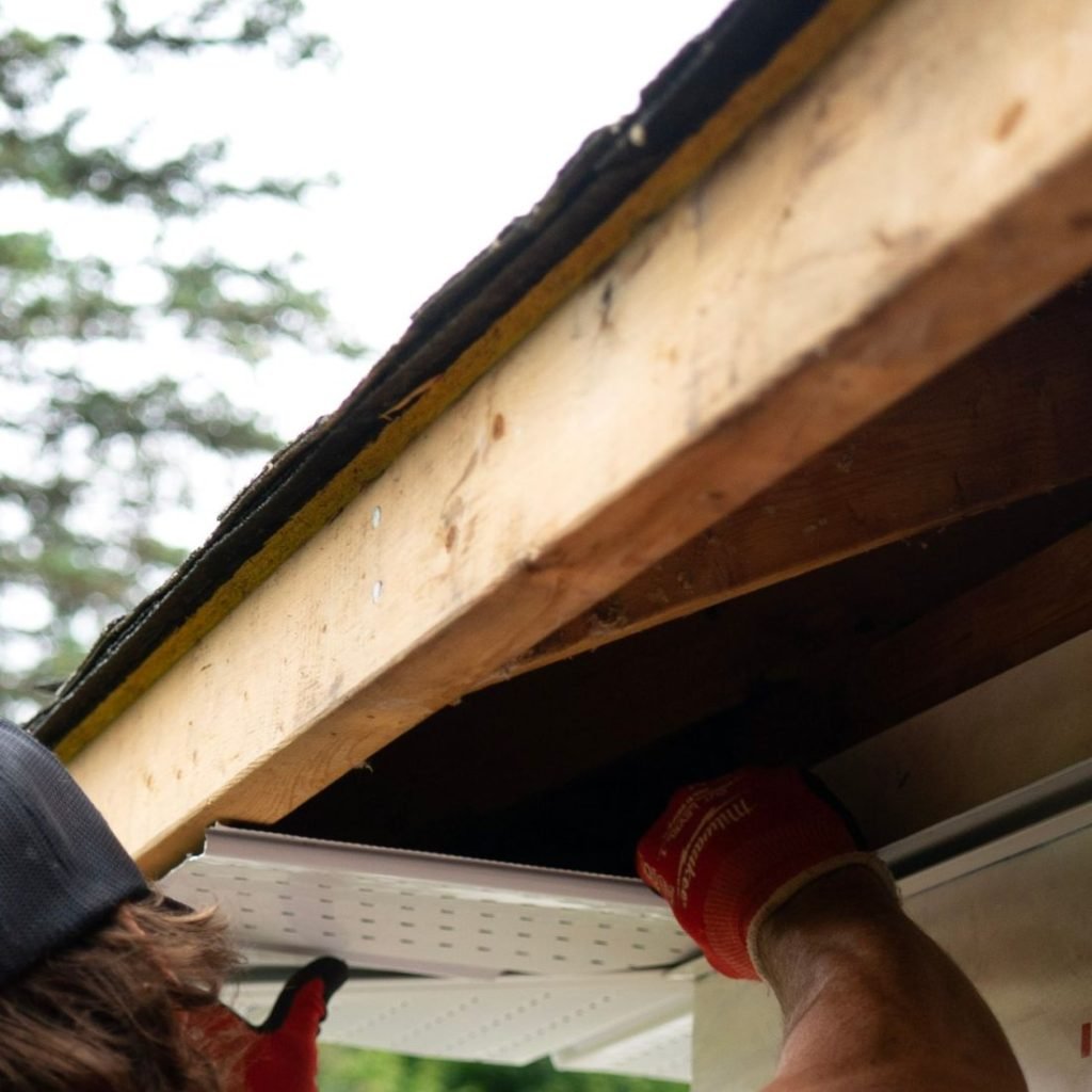 Gloved hands working along the fascia board at the edge of a roof