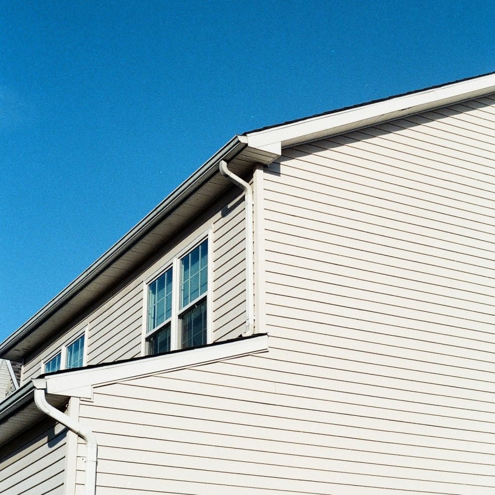 White gutters and downspouts at an inside corner of a newer two-story home with vinyl siding
