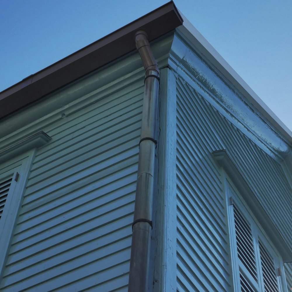 Gutter and downspout running down the corner of an older home with wood siding