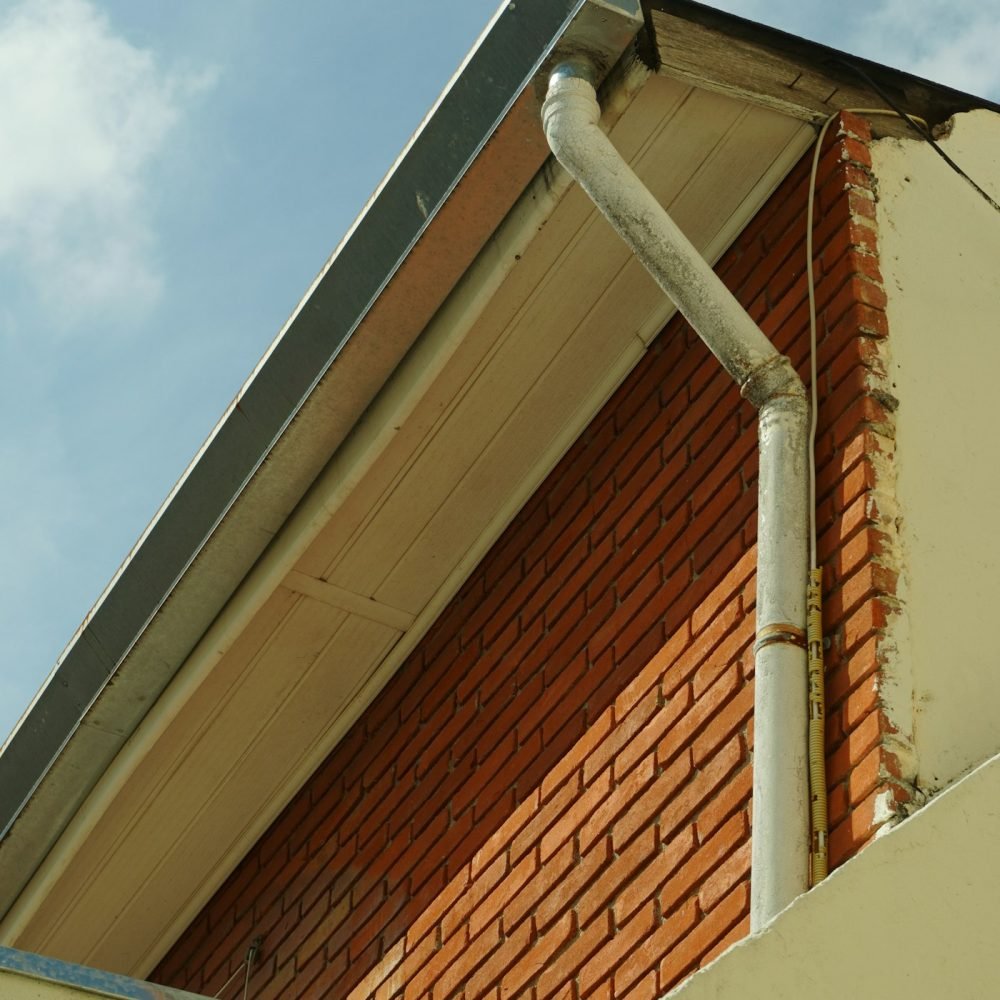 Gutter and downspout running under the roof eave of a tall brick wall