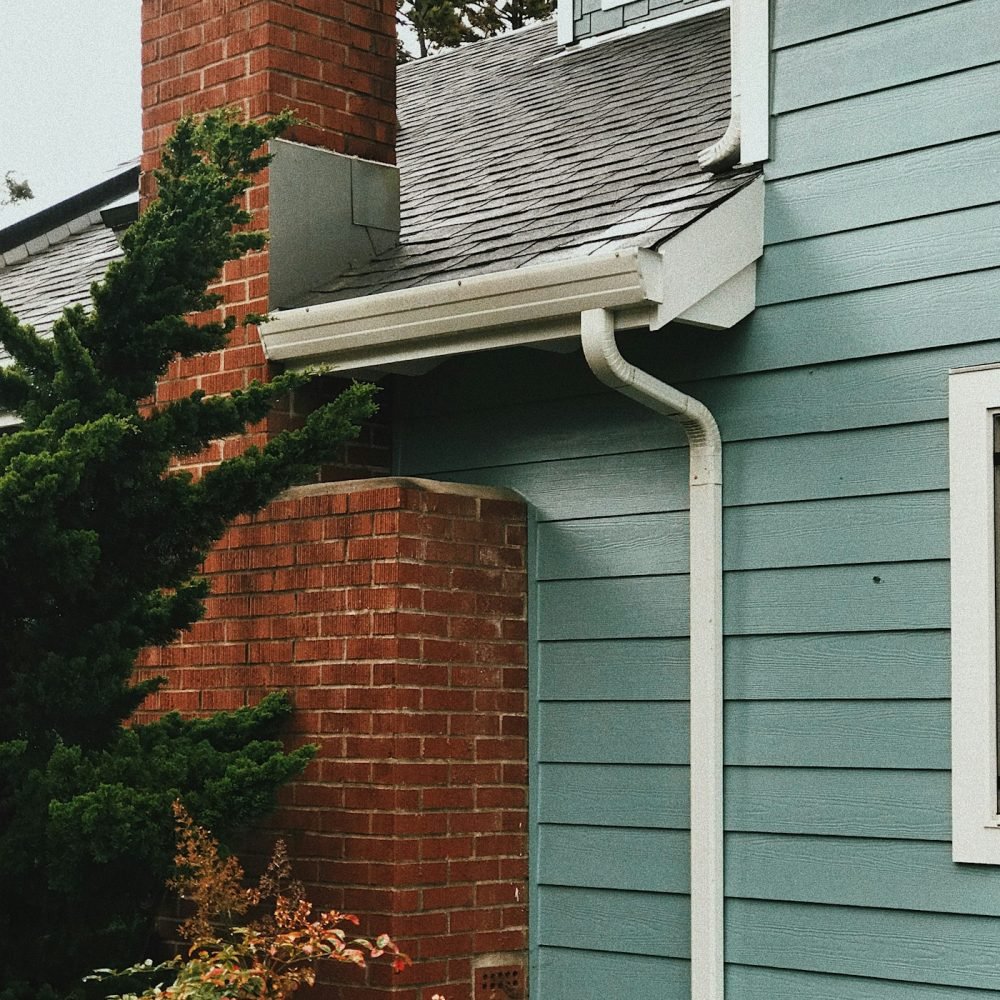 White gutter and downspout on a house with blue siding next to a brick chimney