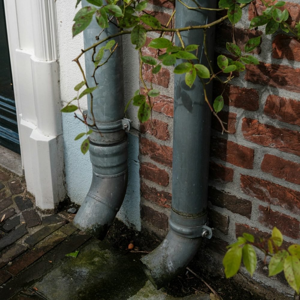 Two downspouts ending at the base of an older brick wall