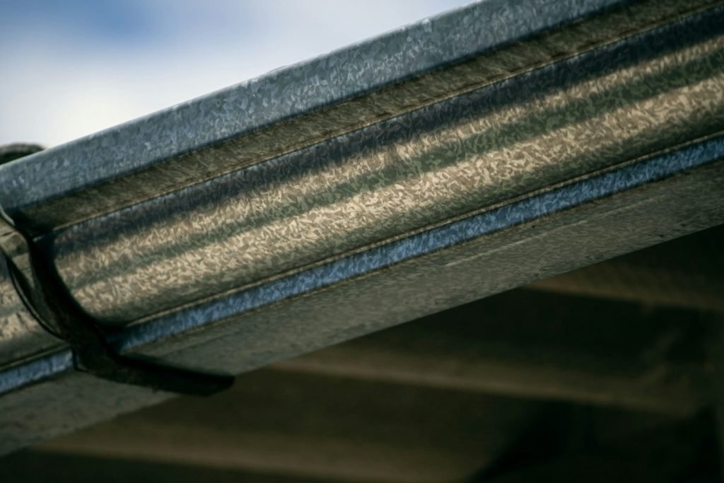 Metal gutter fastened to the roof edge with a strap hanger
